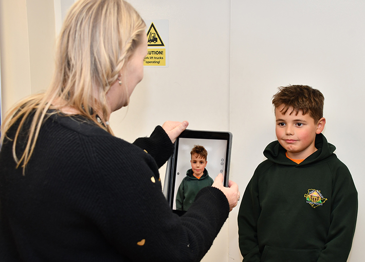 A woman taking a picture of a young boy on an ipad.